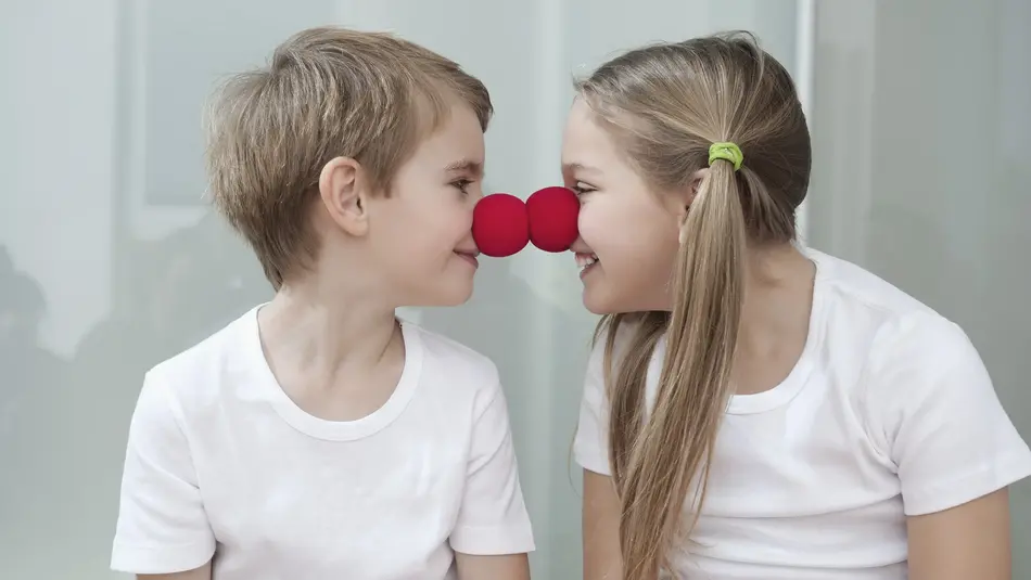 Zwei Kinder mit Clownsnasen Junge und Mädchen mit Clownsnasen, die sich Nasenspitze an Nasenspitze angrinsen