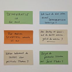 Ein Plakat der Jugendberufshilfe Fechenheim mit sechs Fragen zur Demokratie, darunter „Wo hast du dich schon einmal demokratisch beteiligt?“, „Folgst du politischen Inhalten auf Social Media?“ und „Woher bekommst du Infos über politische Themen?“.
